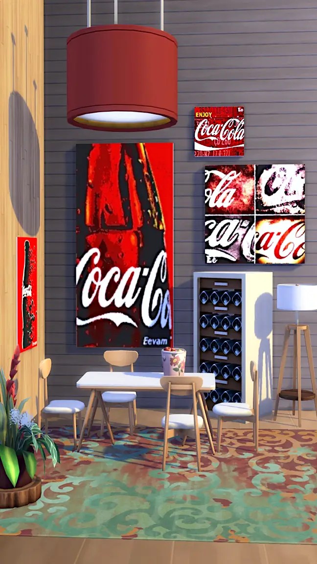 A modern dining area featuring a white table and four wooden chairs, with a decorative flower pot. The walls are adorned with multiple Coca-Cola artworks, including a large poster and smaller framed images. A wine rack is visible beside the table, and a stylish lamp hangs from the ceiling.