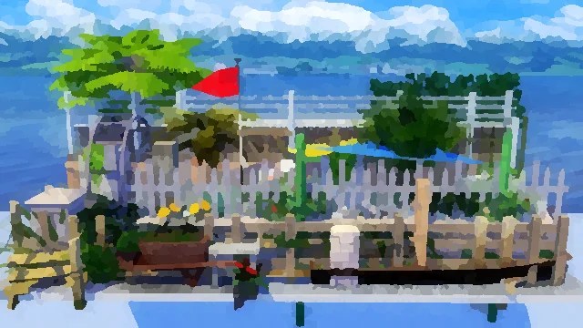 A vibrant outdoor garden area featuring a variety of plants, trees, and flowers, surrounded by a white picket fence. A red flag flutters in the breeze, and colourful umbrellas provide shade. The background shows a scenic view of water and distant mountains under a clear blue sky.